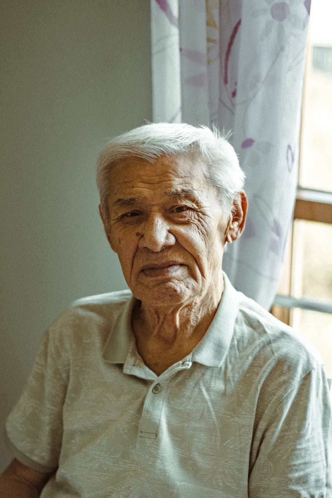 An older man with white hair sitting by a bright window at home